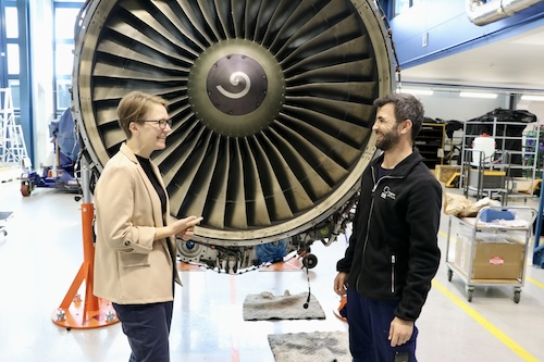 Woman and a man infront of a jet engine smiling. 